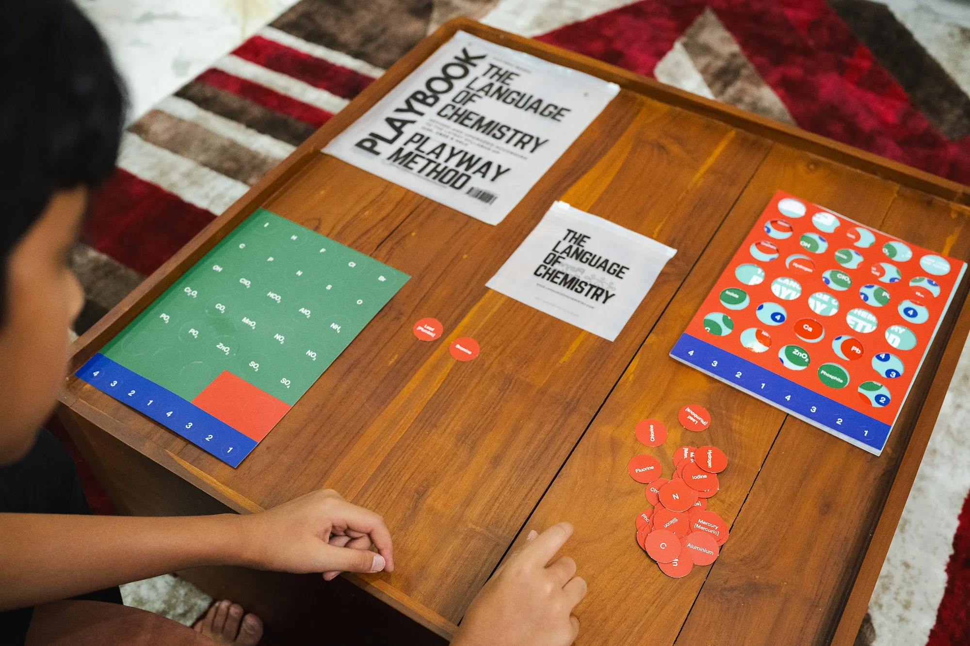 The book’s cover with the red element sheet and green radical sheet laid out beside it, and loose tokens scattered across the table.